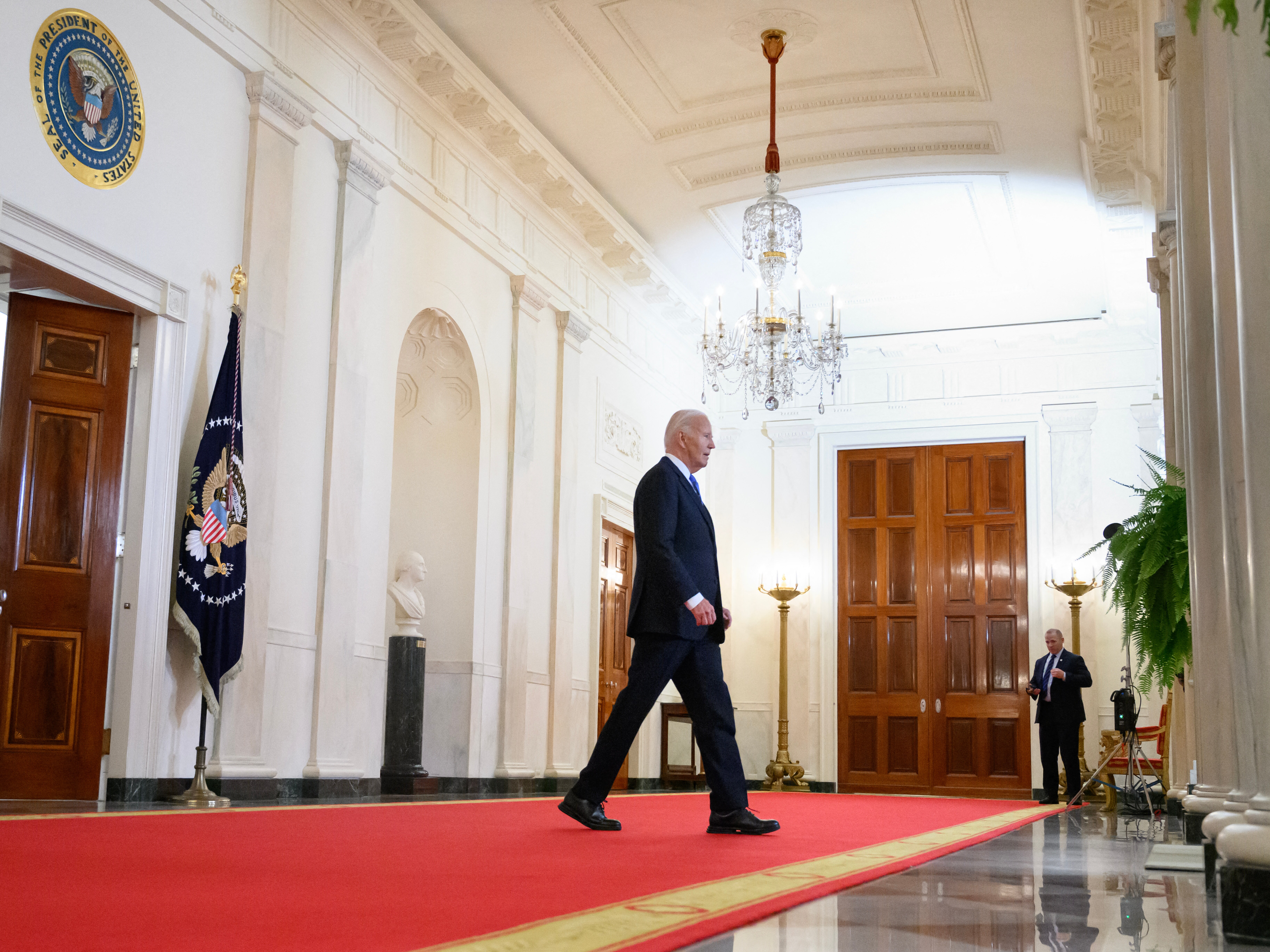 caption: President Biden walks through the Cross Hall of the White House on July 1.