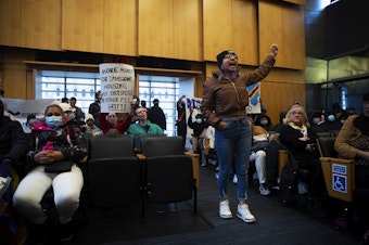 caption: Rosario Lopez leads a chant in council chambers following public comment after asylum seekers, activists and allies marched to Seattle City Hall to ask for assistance with housing on Tuesday, February 27, 2024, in Seattle. Seattle city council members abruptly left council chambers. 
