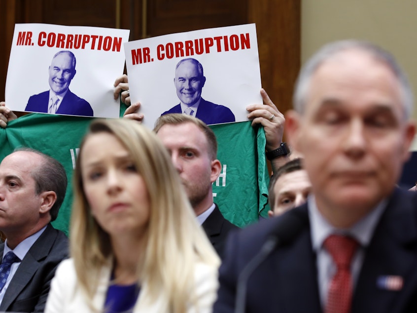 caption: Protesters hold up signs and shirts behind then-Environmental Protection Agency Administrator Scott Pruitt while testifying on Capitol Hill in April. Pruitt was one of a handful of Trump administration officials forced to resign while facing ethics investigations this year.