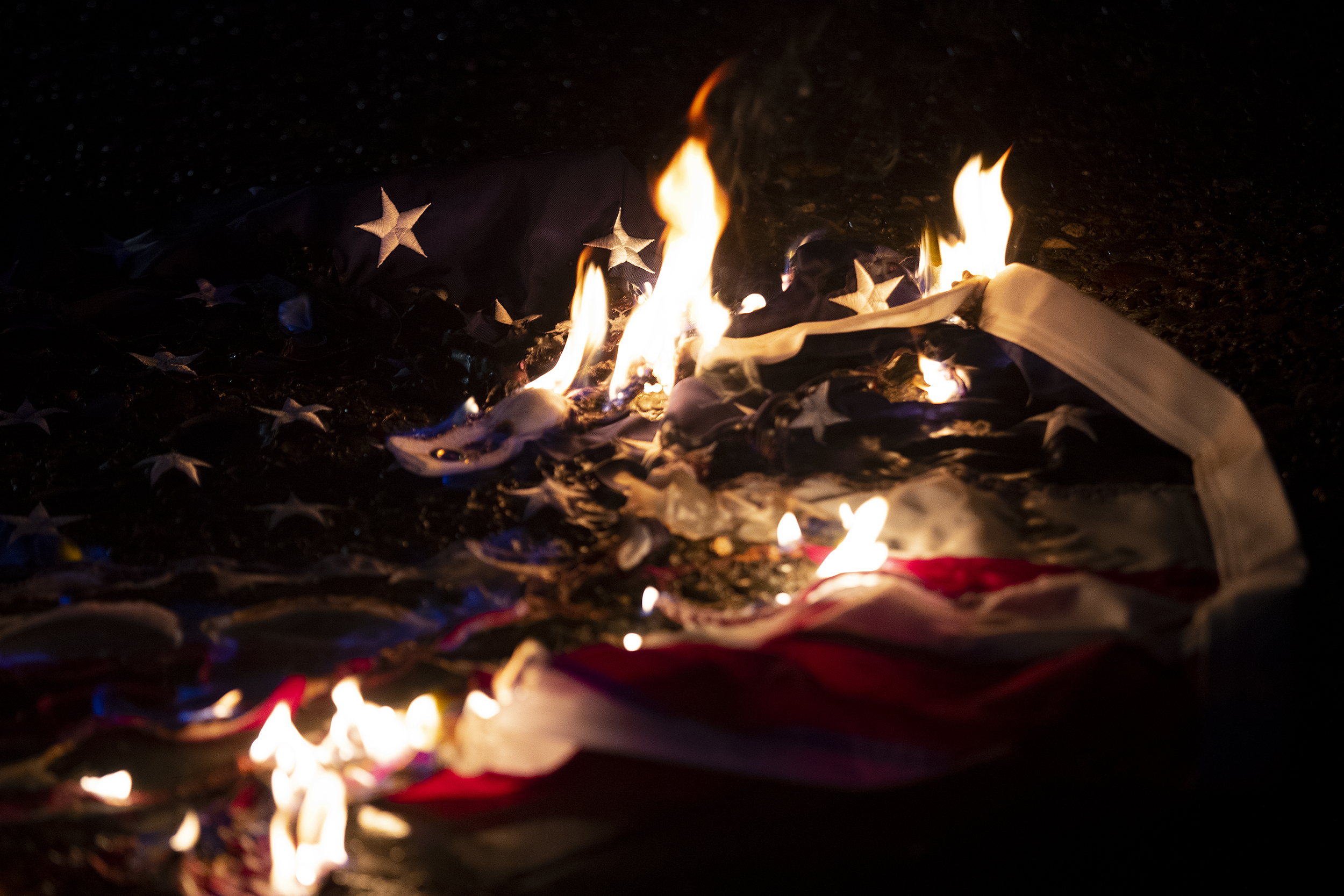 caption: Protesters set fire to an American flag following a vigil honoring Renee Nicole Good on Thursday, January 8, 2026, at Pier 58 in Seattle. 