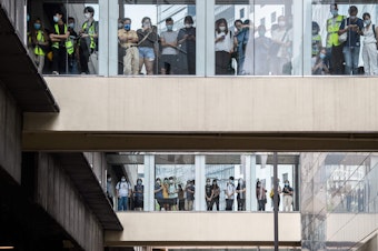caption: Bystanders watch from footbridges Wednesday as riot police stand guard below outside a building in Hong Kong.