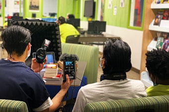caption: Three teens get ready to record an interview in the library at the Judge Patricia H. Clark Children and Family Justice Center during a RadioActive podcasting workshop on April 15, 2021.