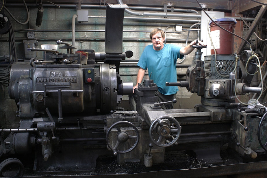 caption: Metal fabricator Denny Jensen with a metal lathe, one of the many old machines he restored and uses at the old Fenpro building in Ballard.