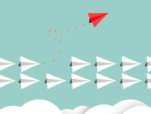 Two rows of white paper airplanes fly in a straight line. One red airplane flies away from the rows with a twirling red dotted line in its wake, to signify breaking from work culture.
