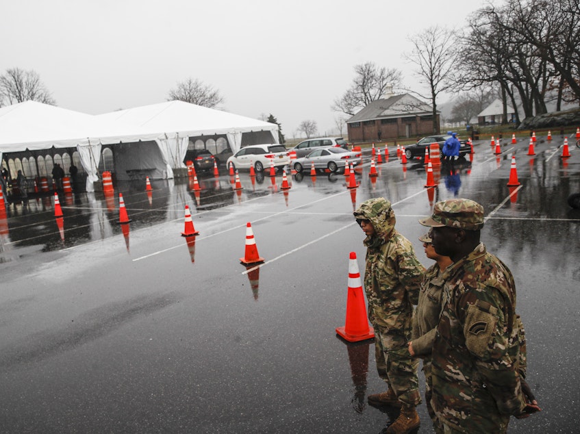 caption: National Guard personnel stand beside a line of motorists waiting for COVID-19 coronavirus infection testing New Rochelle, N.Y., on Friday.