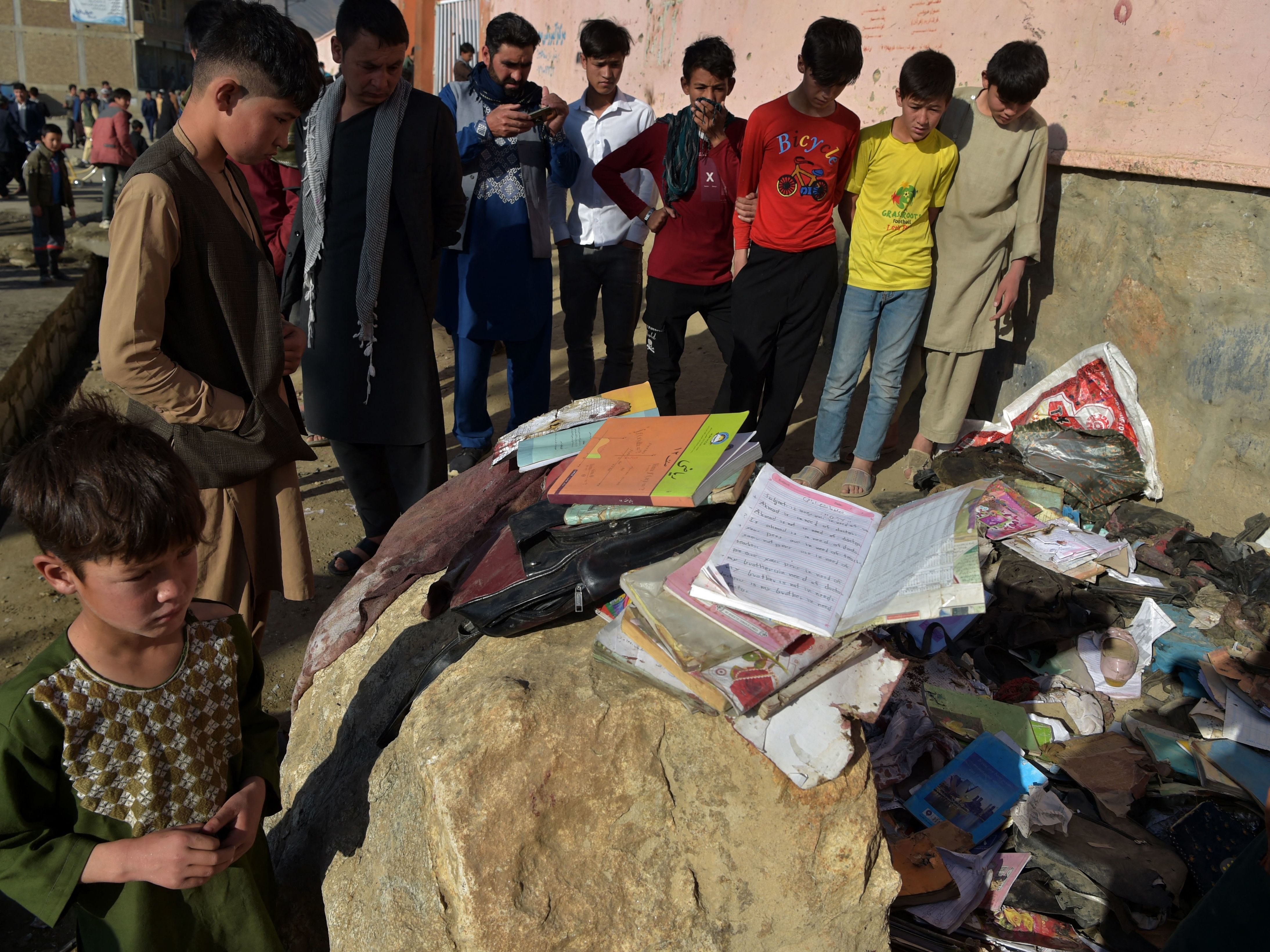 caption: Onlookers stand next to the backpacks and books of victims of the bombing Saturday in Kabul. Most of the victims were teenage schoolgirls.