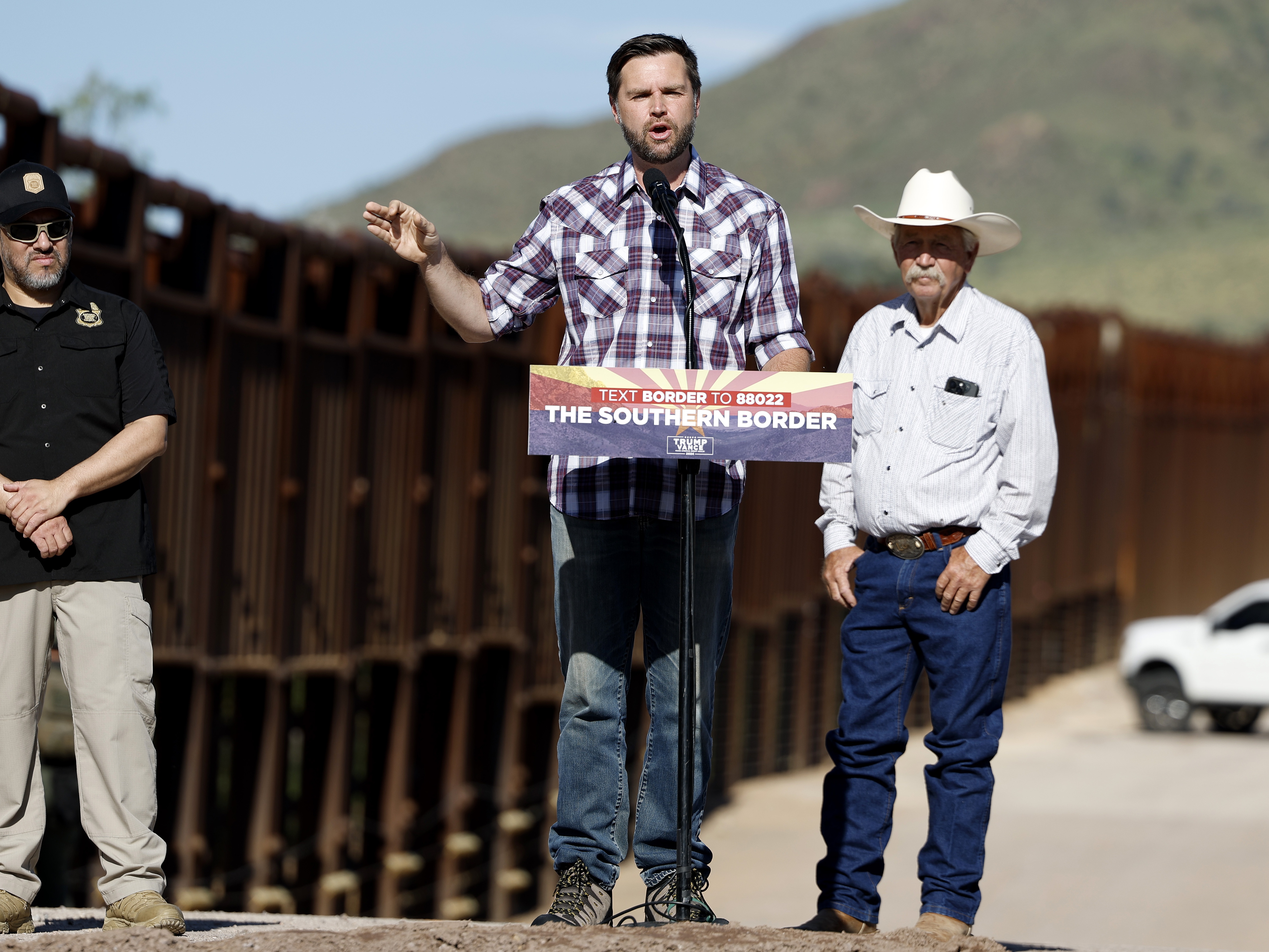 caption: Republican vice presidential nominee Sen. JD Vance of Ohio delivers remarks alongside rancher John Ladd (right) and Paul A. Perez, president of the National Border Patrol Council, as Vance tours the U.S. Border Wall on Thursday in Montezuma Pass, Ariz. Vance is visiting the border on the final stop of his first visit to the Southwest as a vice presidential candidate. 