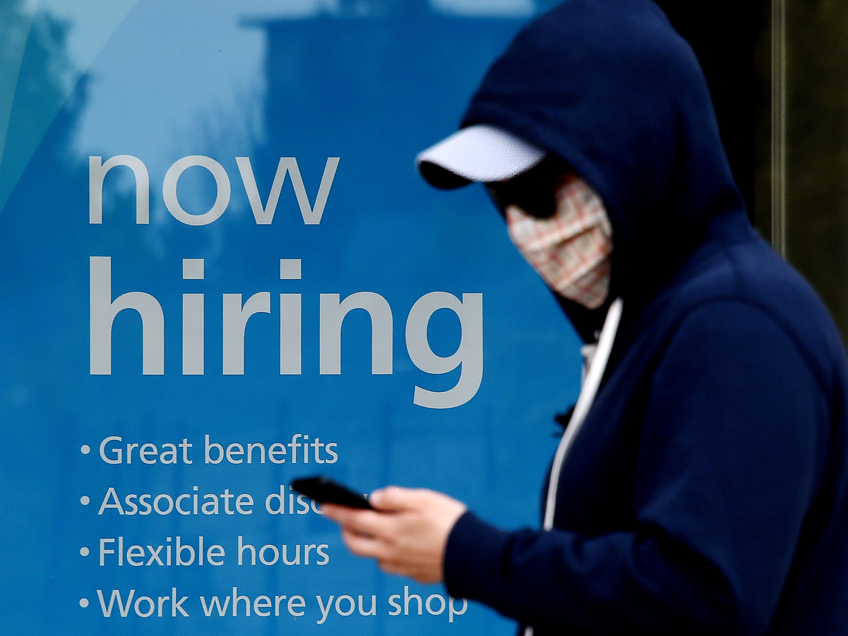 caption: Millions of gig workers have come to depend on a government lifeline that's set to expire at the end of the year. Above, a man wearing a face mask walks past a sign saying "now hiring" on May 14 in Arlington, Va.