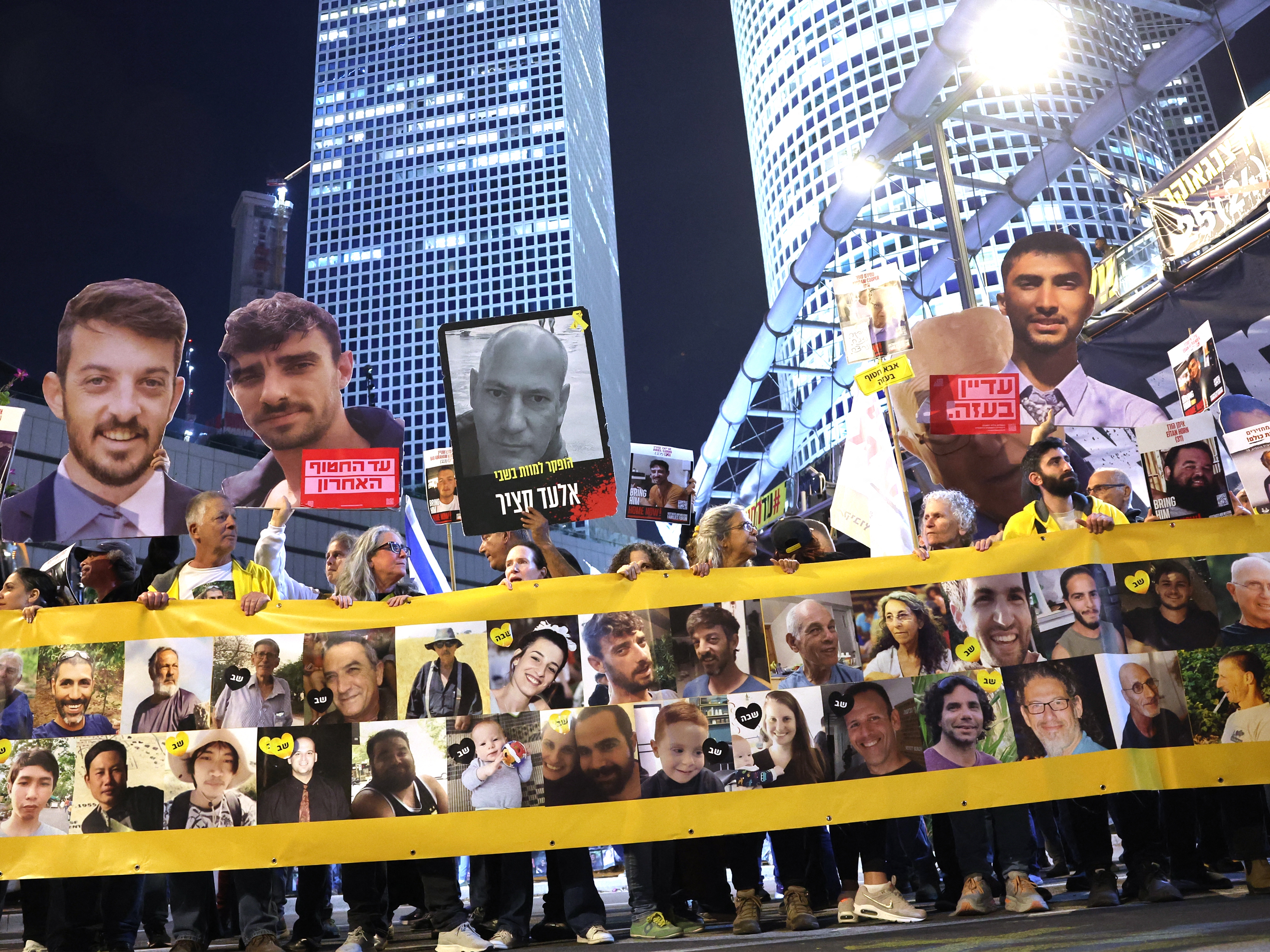 caption: Friends and relatives of Israeli hostages held captive since the October 7, 2023 attacks by Palestinian militants in the Gaza Strip, stand behind a banner bearing their portraits during a demonstration calling for action to secure their release in front of the Israeli Defense Ministry in Tel Aviv on Tuesday.