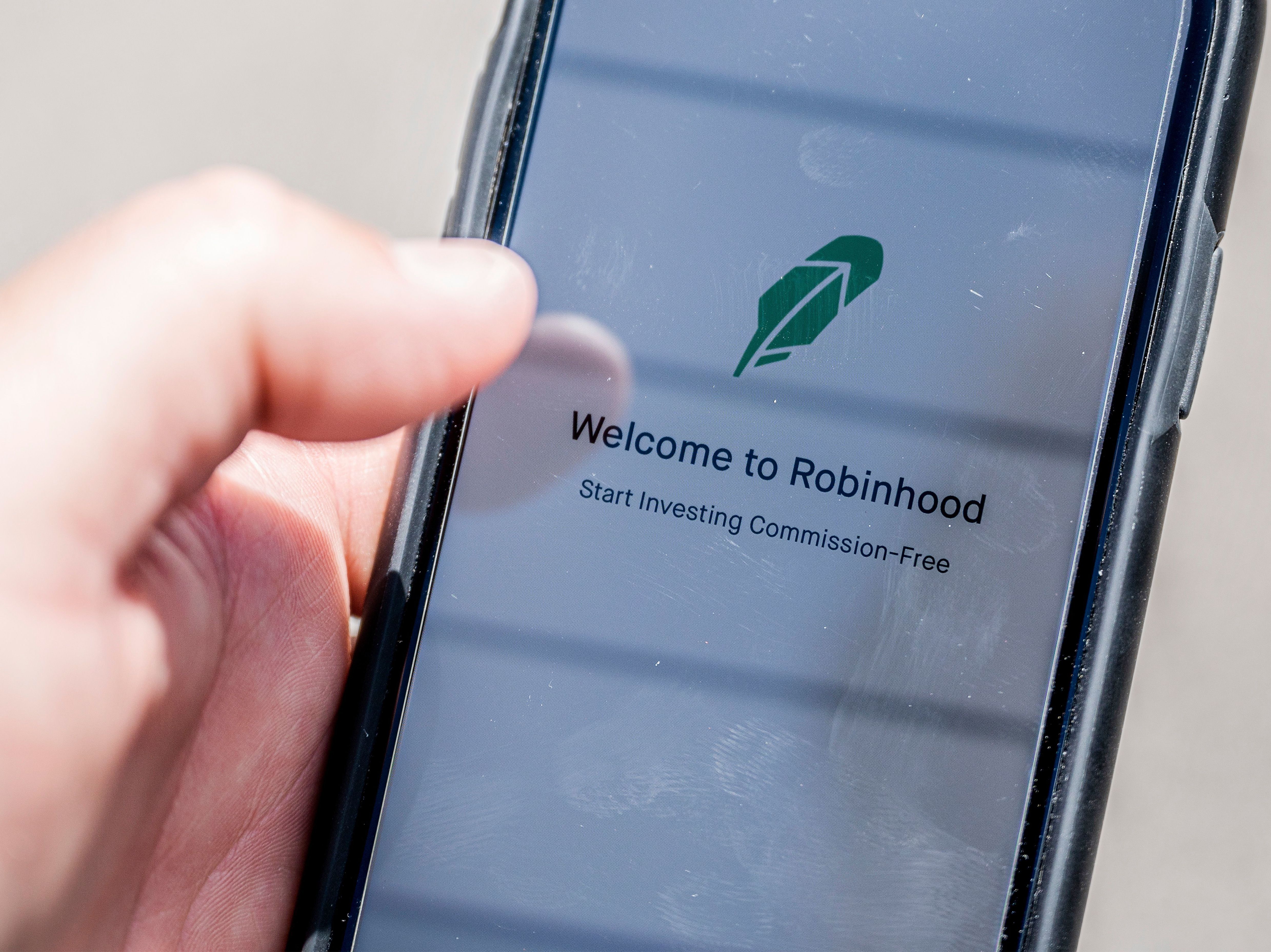 caption: The Robinhood investment app appears on a smartphone in this photo illustration. Day trading has surged during the coronavirus pandemic as stay-at-home people try buying and selling stocks, often for the first time.