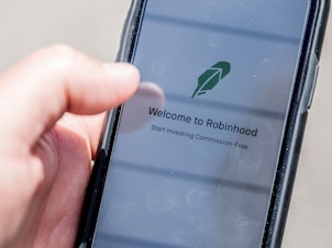 caption: The Robinhood investment app appears on a smartphone in this photo illustration. Day trading has surged during the coronavirus pandemic as stay-at-home people try buying and selling stocks, often for the first time.
