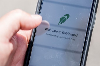 caption: The Robinhood investment app appears on a smartphone in this photo illustration. Day trading has surged during the coronavirus pandemic as stay-at-home people try buying and selling stocks, often for the first time.