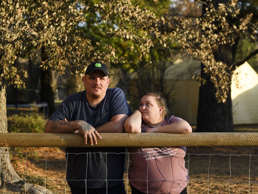 caption: Army veteran Raymond Queen stands with his wife Rebecca Queen outside their home in Bartlesville, Okla.