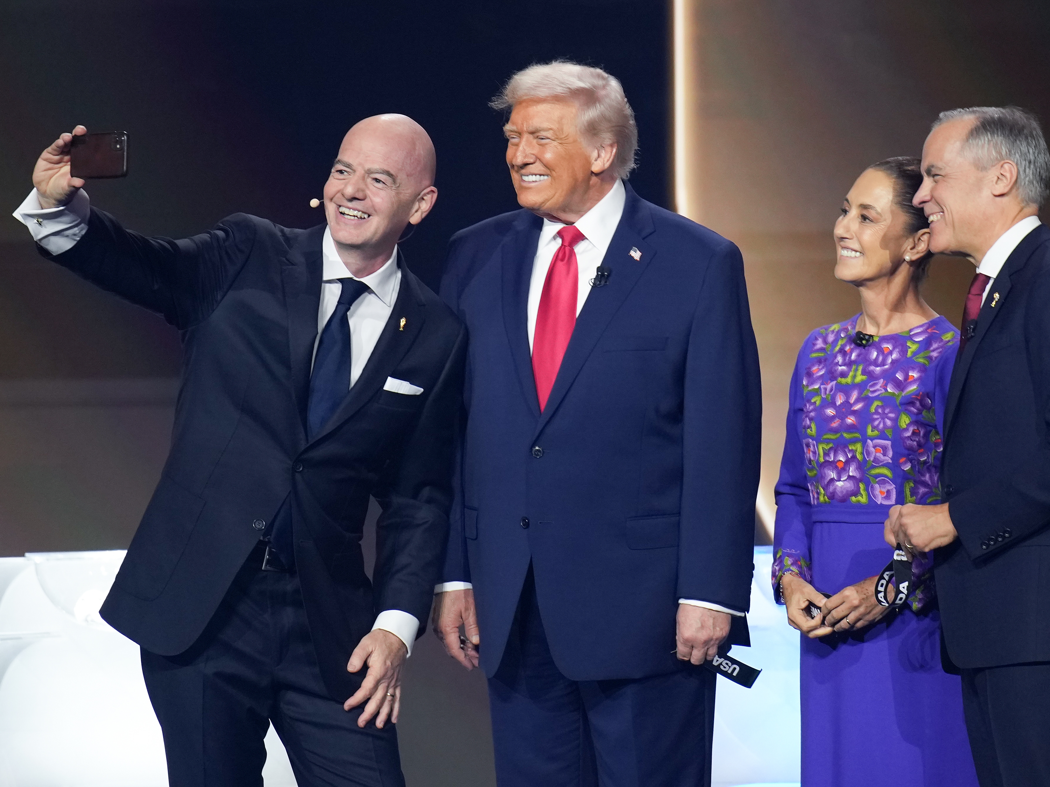 caption: FIFA President Gianni Infantino (left) takes a selfie with President Trump, Mexican President Claudia Sheinbaum, and Canadian Prime Minister Mark Carney during the FIFA World Cup 2026 Official Draw at the John F. Kennedy Center for the Performing Arts in Washington, D.C., on Dec. 5, 2025.