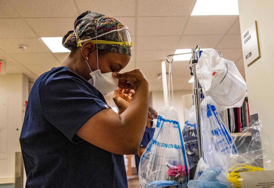 caption: A medical worker puts on a mask before entering a negative pressure room with a COVID-19 patient in the ICU ward at UMass Memorial Medical Center in Worcester, Mass., last week.