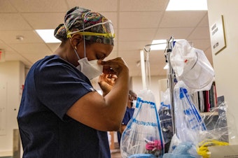 caption: A medical worker puts on a mask before entering a negative pressure room with a COVID-19 patient in the ICU ward at UMass Memorial Medical Center in Worcester, Mass., last week.