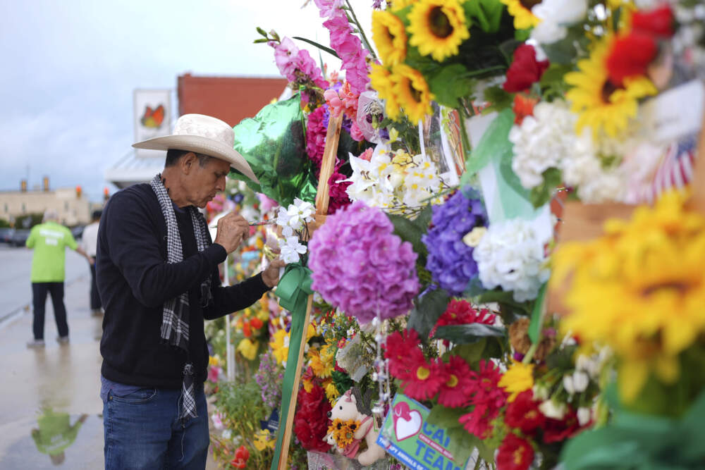 caption: Roberto Marquez paints names on a cross at a memorial wall for flood victims, Sunday, July 13, 2025, in Kerrville, Texas. (Eric Gay/AP)