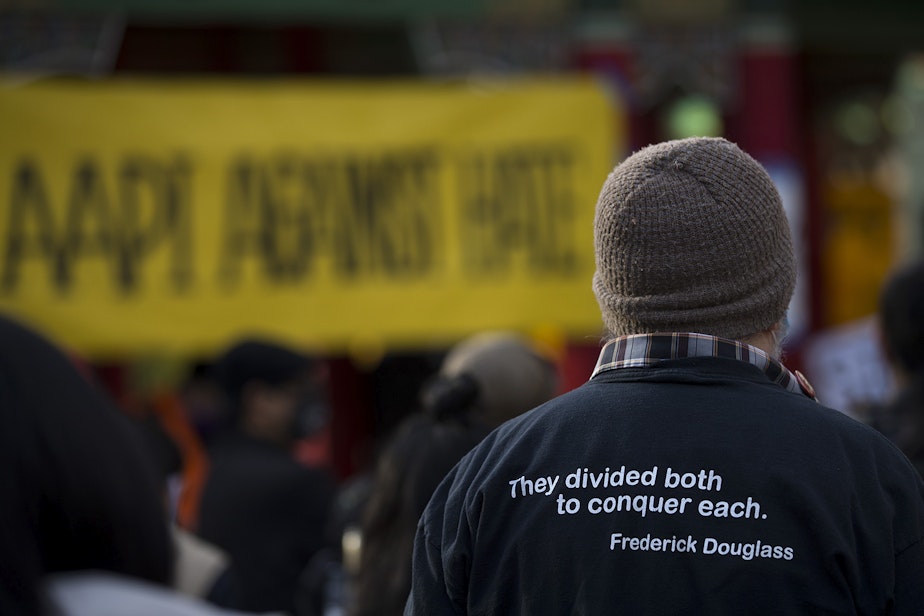 caption: A person wearing a shirt that includes a quote from Federick Douglass, "they divided both to conquer each," listens to speakers as hundreds gathered for the 'We Are Not Silent' rally and march against anti-Asian hate and violence on Saturday, March 13, 2021, at Hing Hay Park in Seattle. Several days of actions are planned by rally organizers in the Seattle area following recent attacks and violence against Asian American and Pacific Islander communities.
