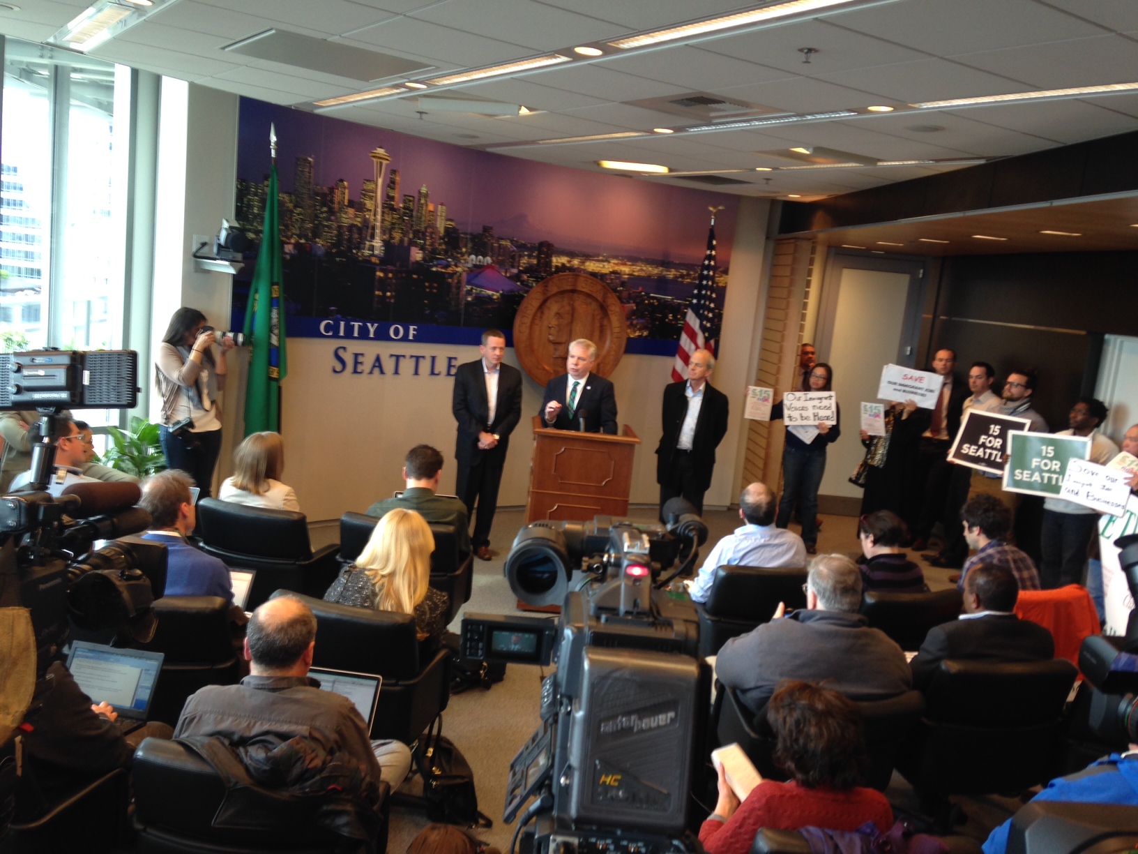 caption: Mayor Ed Murray addresses the press on Thursday afternoon, flanked by demonstrators on both sides of the minimum wage debate. 