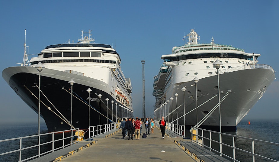 caption: People walking down a pier between two large cruise ships.