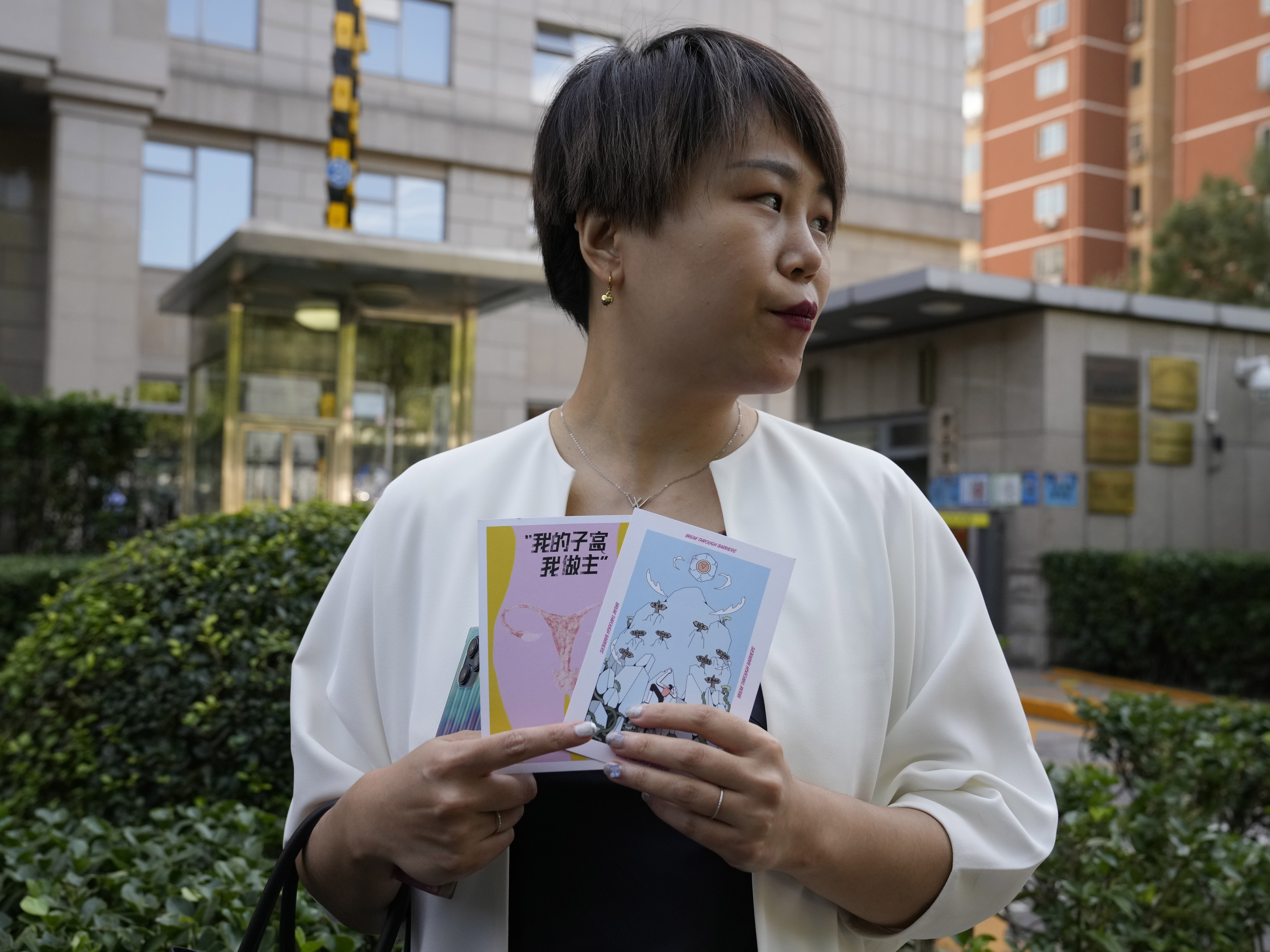 caption: Teresa Xu holds up cards, one of which reads "My Womb, My Choice," before attending a court session at the Chaoyang People's Court in Beijing, Sept. 17, 2021. Xu is suing a public hospital for the right to freeze her eggs after it refused to do so because she isn't married.