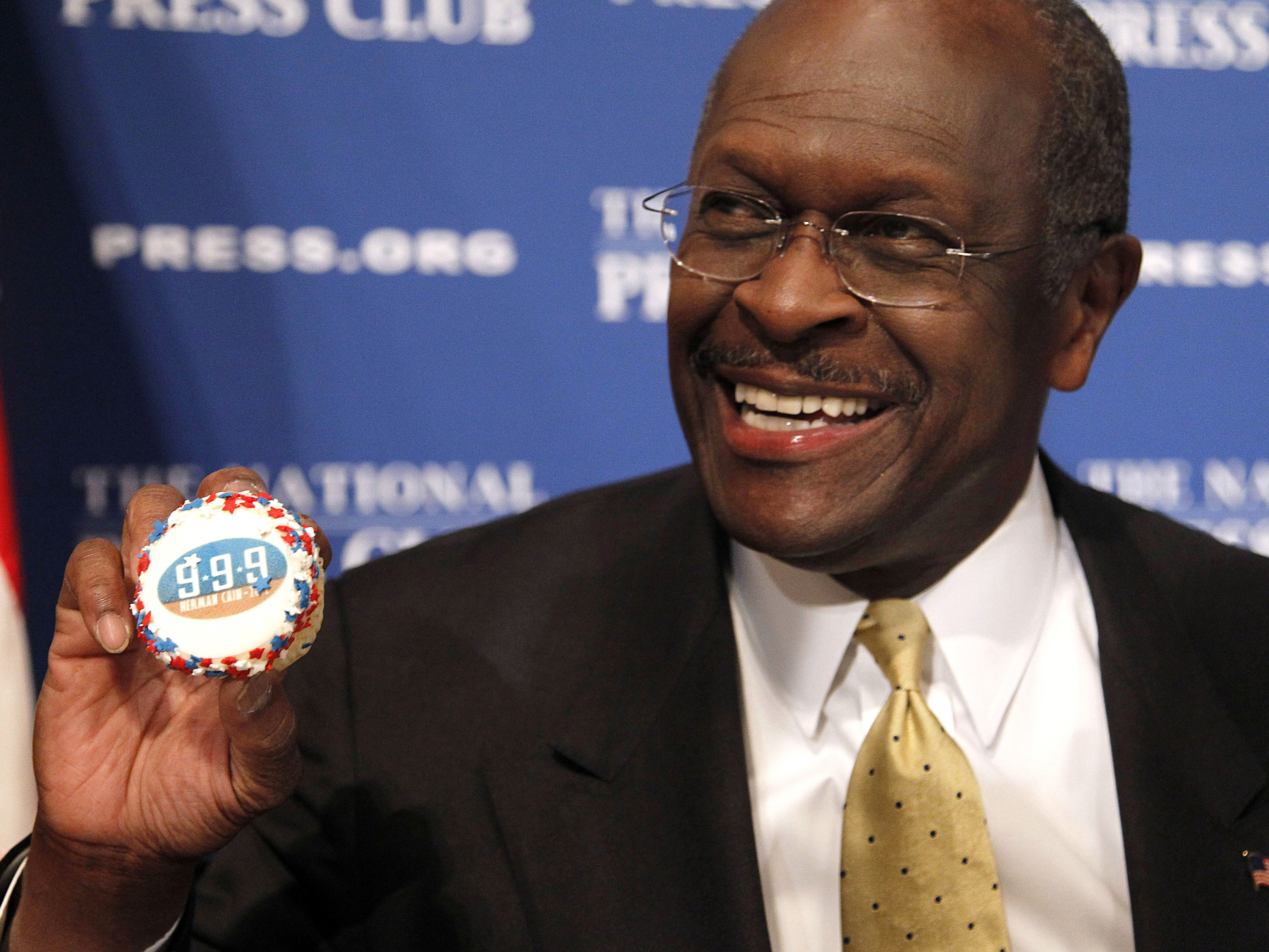 caption: Herman Cain, then a GOP presidential candidate, holds a muffin bearing his catchphrase "9-9-9" tax plan at the National Press Club in Washington in 2011. Cain's death was announced Thursday.