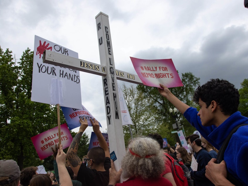 caption: A counter-protestor holds a large cross during a youth pro-abortion rights rally outside of the Supreme Court in Washington, D.C., on May 5, following the leak of a draft Supreme Court opinion to overturn <em>Roe v. Wade</em>.