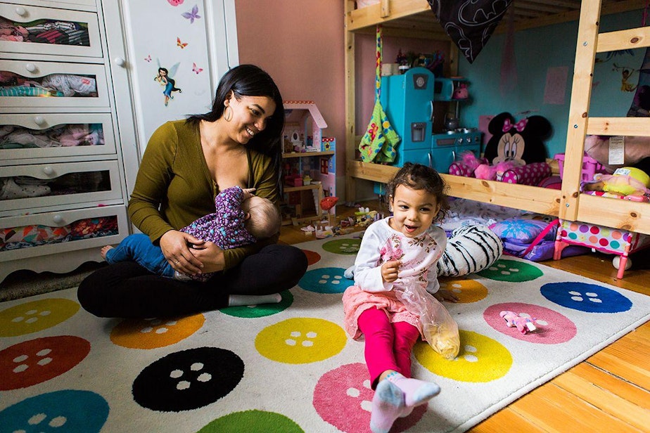 caption: Andrea Arai nurses baby Norah, 8 months, as daughter Milla plays nearby.