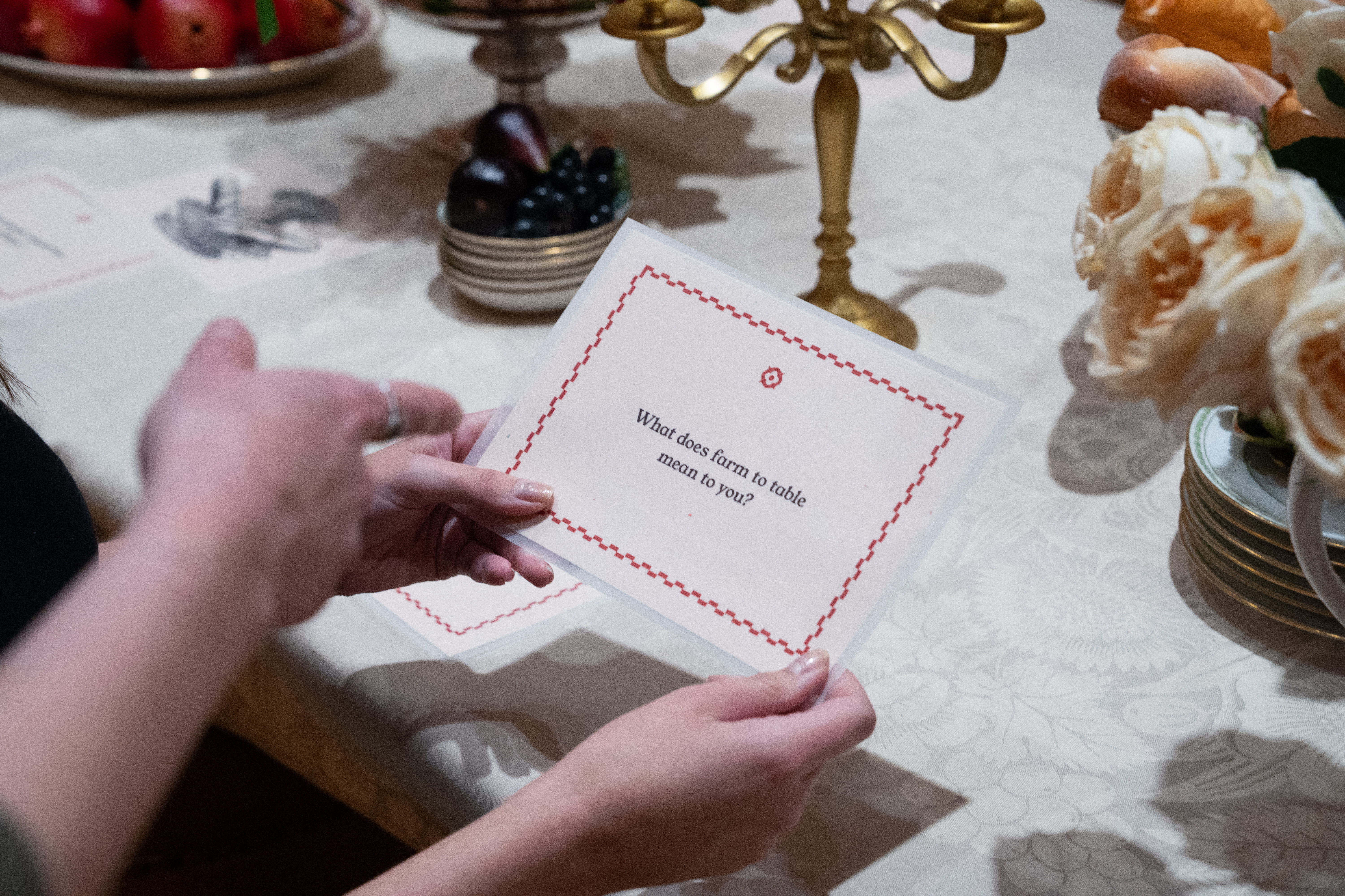 caption: A dining table, with prompt cards tucked between plates, invites visitors to reflect on the exhibition and to spark conversation. 