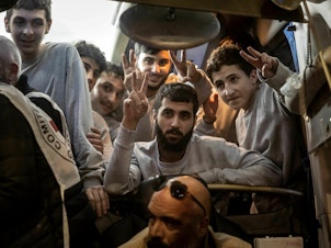 caption: People gesture from a Red Cross bus carrying Palestinian prisoners released from Israeli jails in exchange for hostages released by Hamas from the Gaza Strip, in Ramallah, in the occupied West Bank, on Sunday.