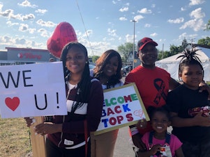 caption: LeCandice Durham, Lenny Lane and their children stand by the Tops parking lot entrance in Buffalo, N.Y., on Friday to welcome back customers and employees on opening day after the supermarket was closed after May's mass shooting.