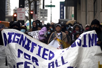 caption: Adriana Figueira, center, leads a group of primarily Venezuelan asylum seekers, once housed at the Sleep Inn in SeaTac, to Seattle City Hall along with activists, mutual aid organizations and allies to ask for further assistance with housing from Seattle city councilmembers on Tuesday, Feb. 27, 2024, in Seattle. 