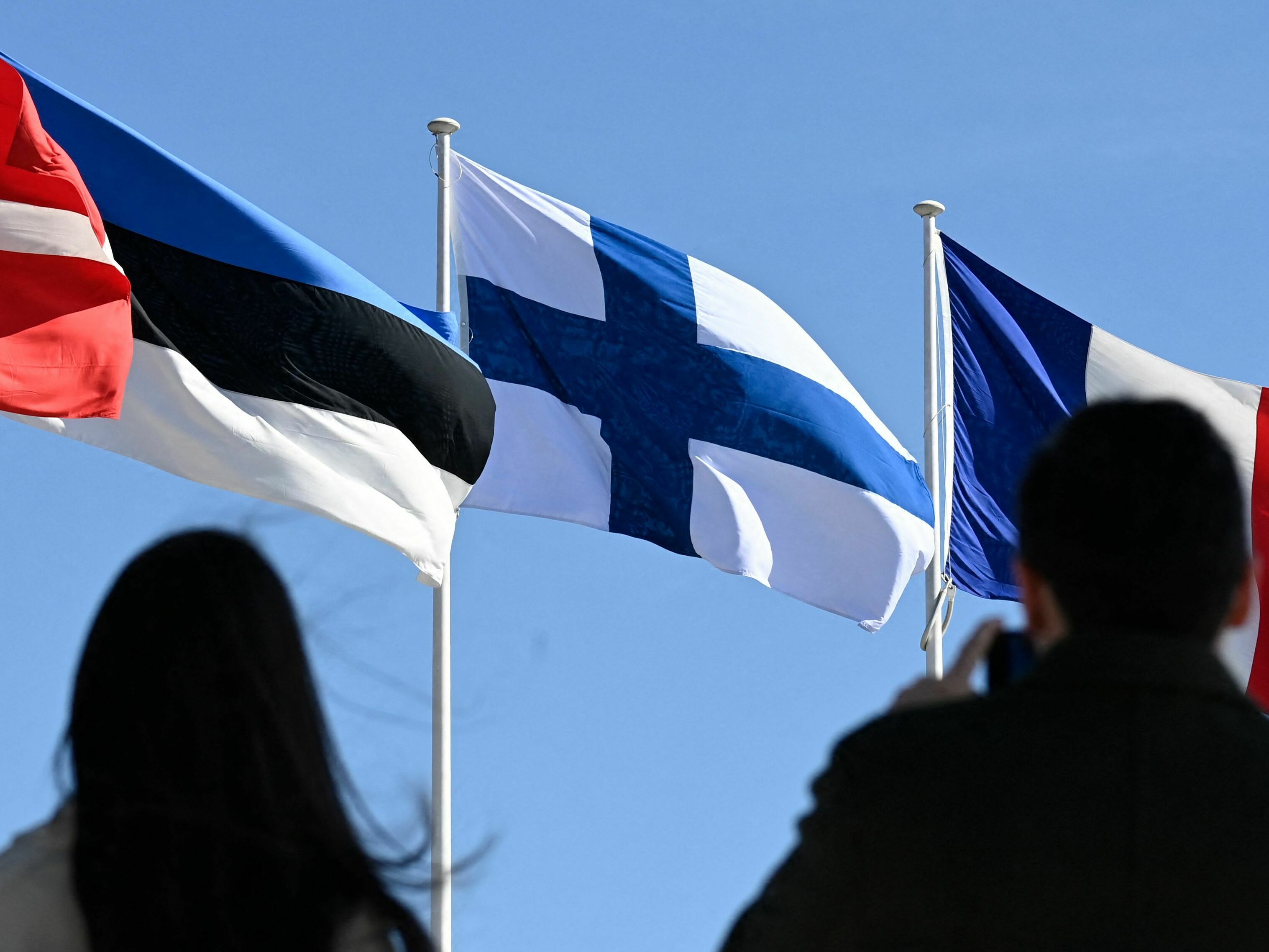 caption: People stand in front of the Finnish national flag after a flag-raising ceremony at the NATO headquarters in Brussels on April 4, 2023.
