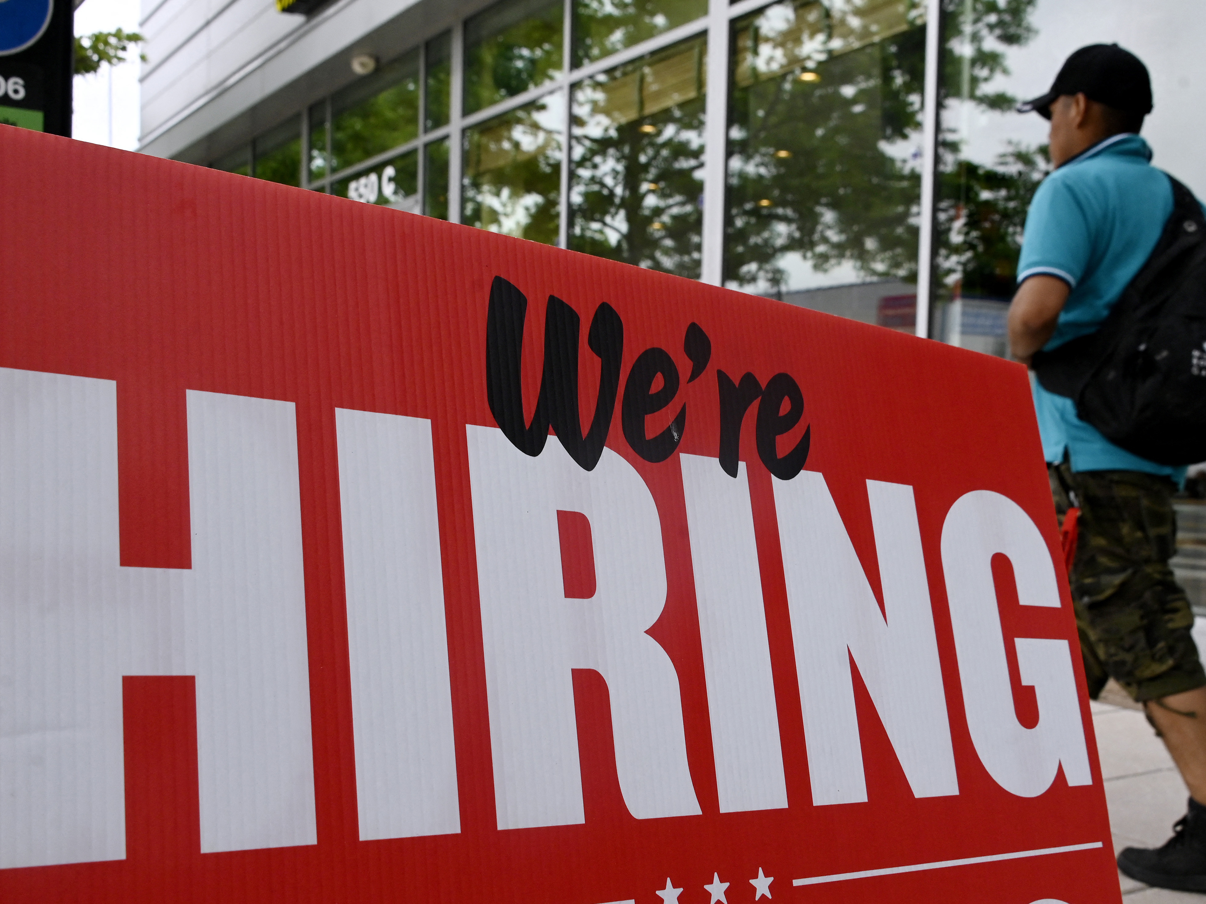caption: Fewer jobs were added in June, but the labor market is still tight. A man walks past a "now hiring" sign posted outside of a restaurant in Arlington, Va., last month.