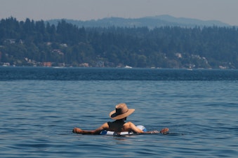 caption: A man floats in Lake Washington at Colman Beach, Monday, June 28, 2021, when the National Weather Service recorded a high temperature of 108 degrees in SeaTac, setting an all-time record for the area.