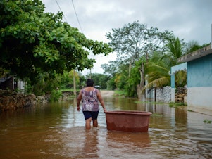 caption: A woman from the Mayan community of Tecoh wades through the water in a flood caused by Tropical Storm Cristobal in the town of Tecoh, near Merida in Yucatan State, Mexico, in June 2020.