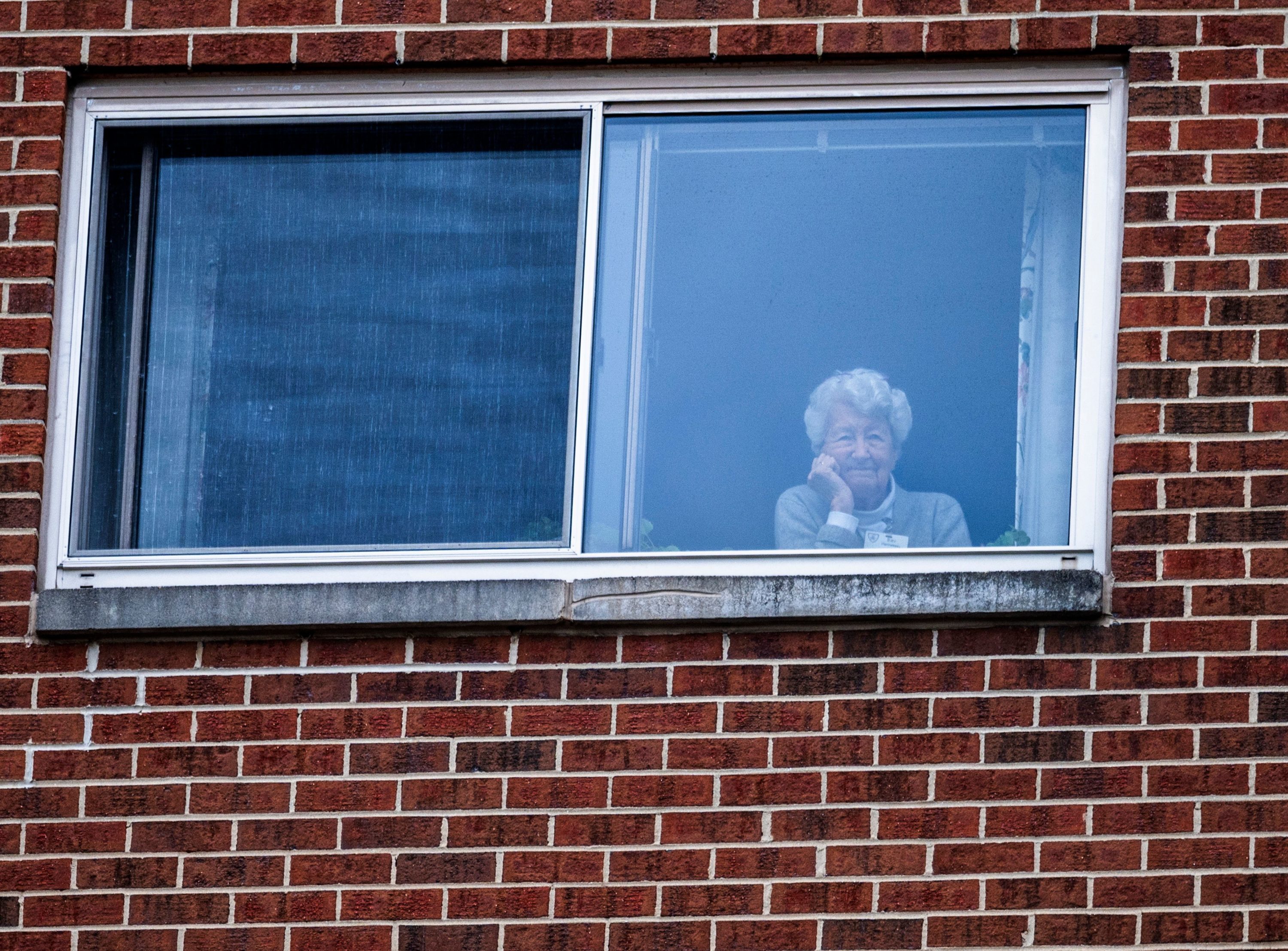 caption: A resident of the Goodwin House senior living community, looks on as she listens to the DC area motown band "The Tribe" play a social distance concert in their parking lot in Arlington, Virginia, during the coronavirus pandemic on April 14, 2020. (ANDREW CABALLERO-REYNOLDS/AFP via Getty Images)