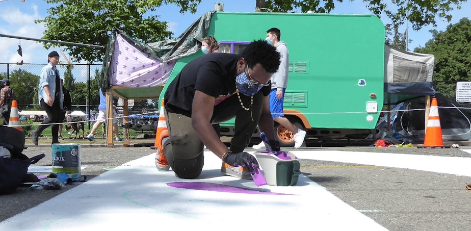 caption: Moses Sun paints in the "M" letter in the BLACK LIVES MATTER letters along Pine Street in Seattle.