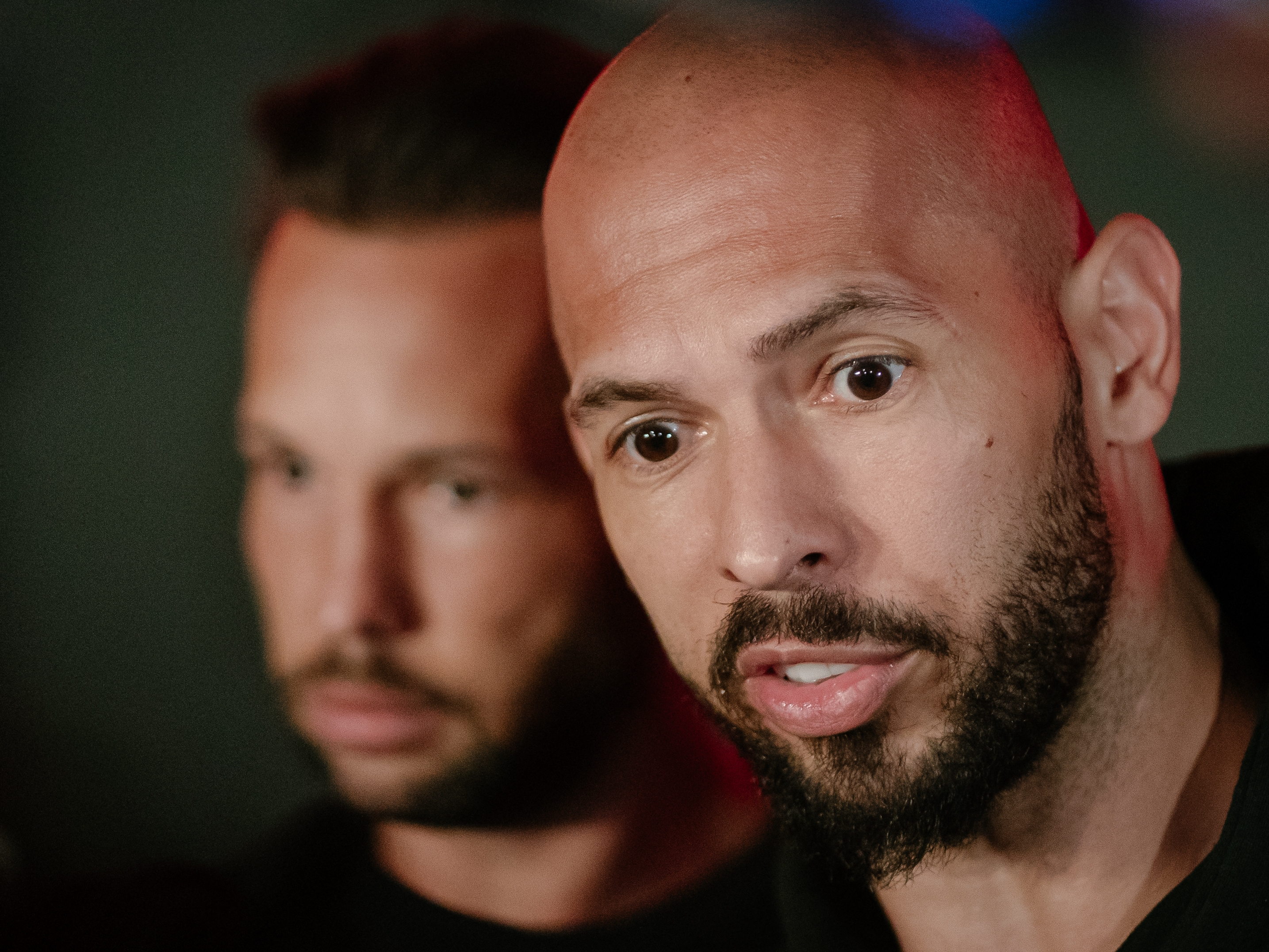 caption: Andrew Tate and his brother Tristan Tate talk to the media outside their residence on March 23, 2025 in Bucharest, Romania.