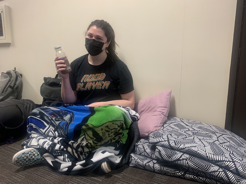 caption: SPU senior Cambria Judd-Babbitt enjoys a coffee after spending another night sleeping on the floor outside interim-President Pete Menjares's office.
 "The fun thing about the sleepovers here is that the lights do not fully turn off," Judd-Babbitt said. "So yesterday someone was kind enough order a bunch of sleep masks, and I think that's how we survived the night."