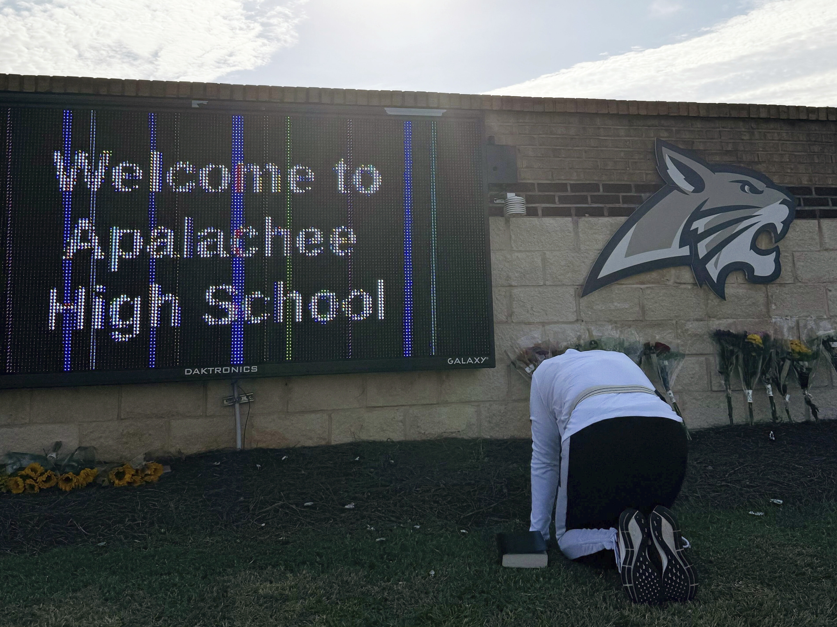 caption: A person kneels in front of flowers placed outside the entrance to Apalachee High School on Thursday, a day after a mass shooting at the school in Winder, Ga.