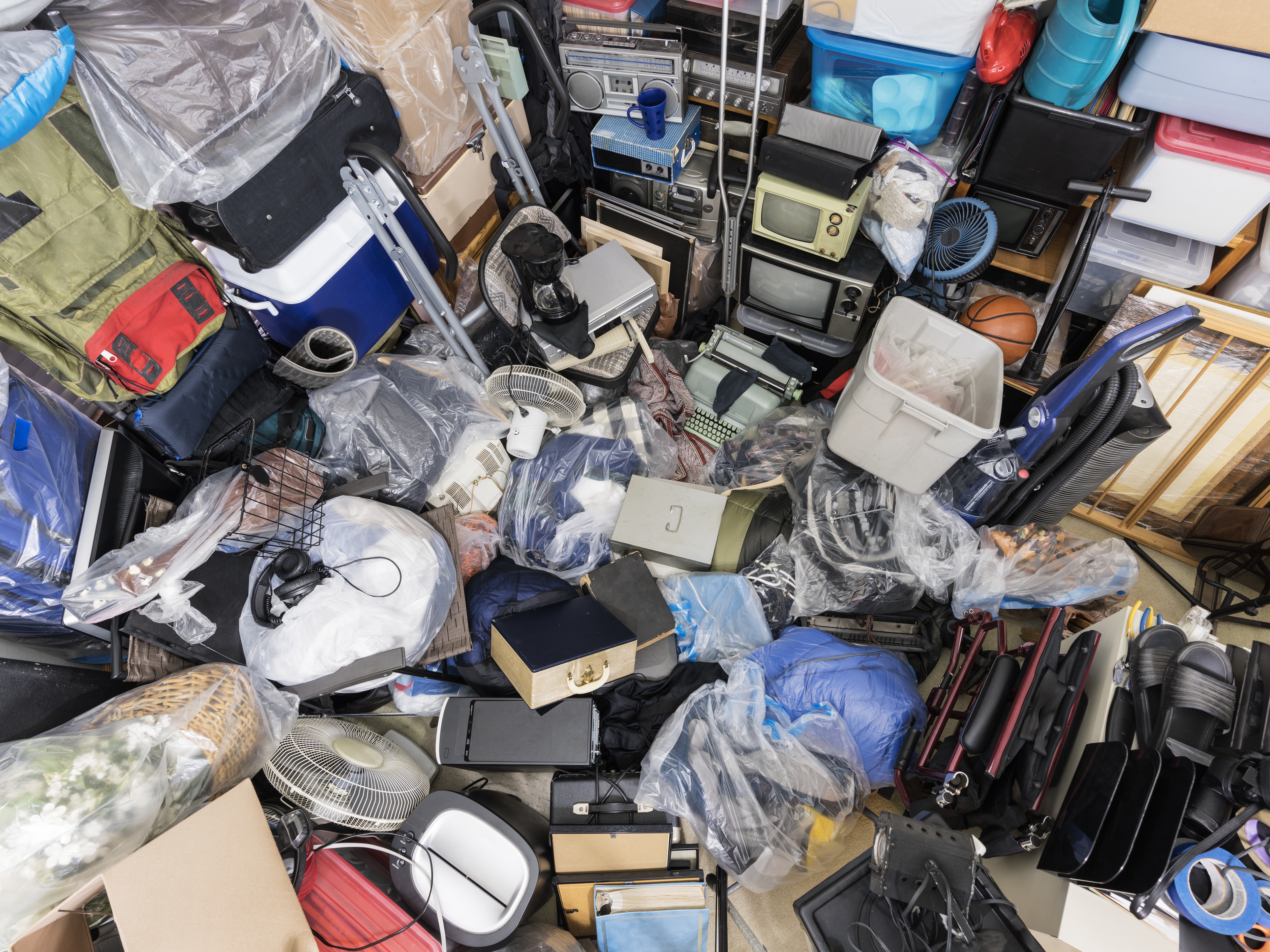 caption: Pile of objects accumulated in someone's home including clothing and outdoor equipment, household objects, and old electronics.