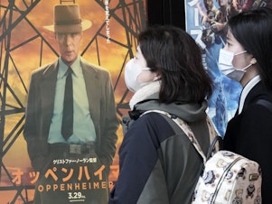 caption: People walk by a poster to promote the movie <em>Oppenheimer</em> on Friday in Tokyo.