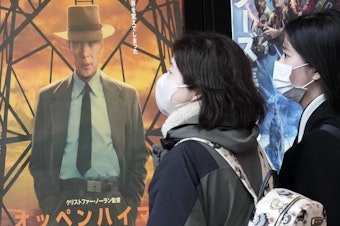 caption: People walk by a poster to promote the movie <em>Oppenheimer</em> on Friday in Tokyo.