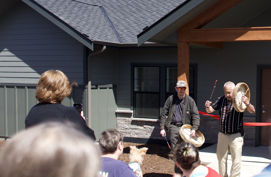 caption: Samish Indian Nation Tribal Chairman Tom Wooten (right) beats a drum at a ribbon cutting ceremony for the tribe's new Xwch'ángteng housing community in Anacortes, Washington on Friday, May 17, 2024.