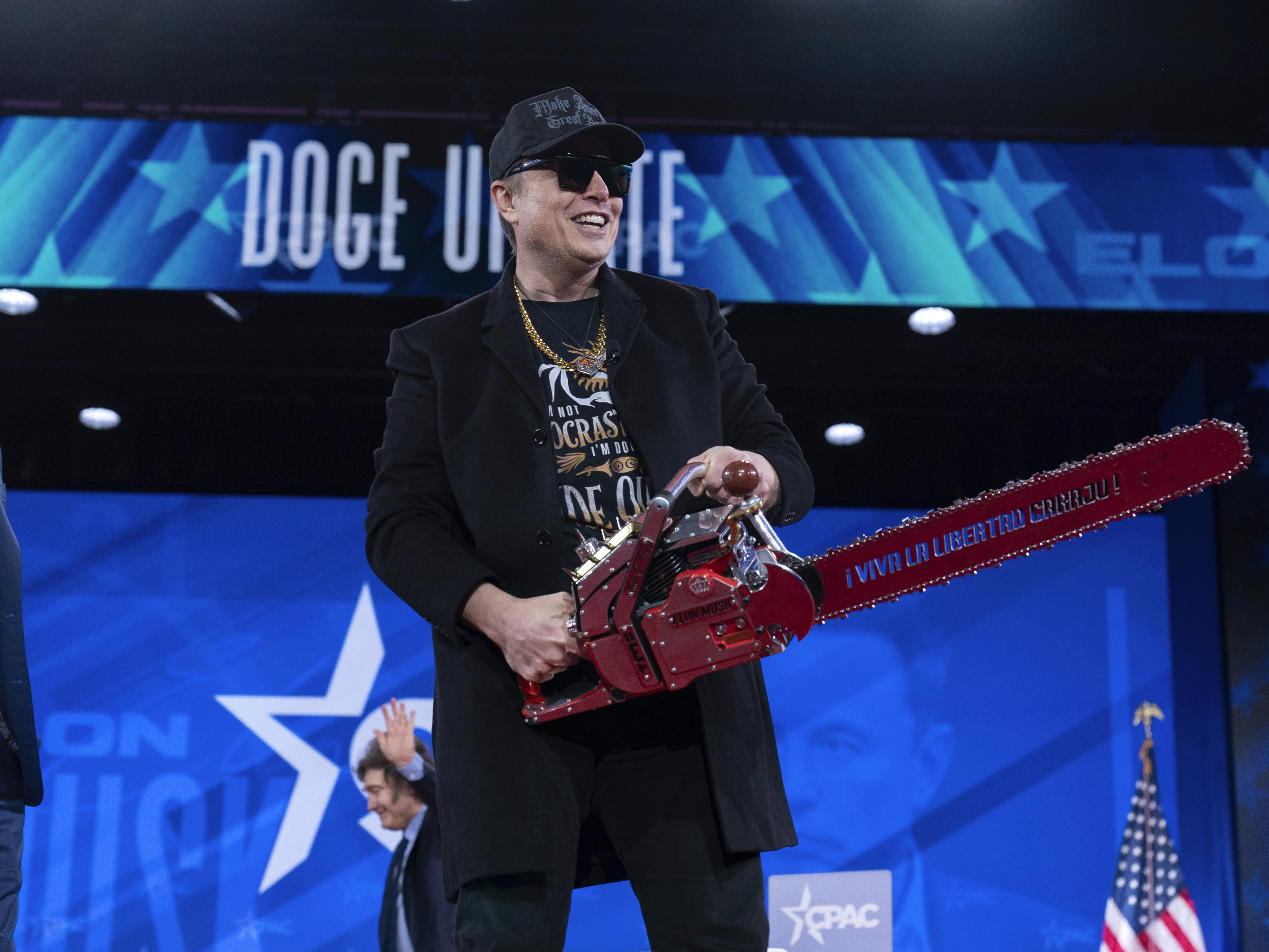 caption: Elon Musk, who oversees the Department of Government Efficiency, or DOGE, holds a chainsaw as he arrives to speak at the Conservative Political Action Conference Thursday in Oxon Hill, Md.