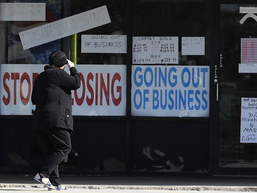 caption: A woman looks at signs at a store in Niles, Ill., on May 13. Shutdowns related to the coronavirus pandemic have left tens of millions out of work.