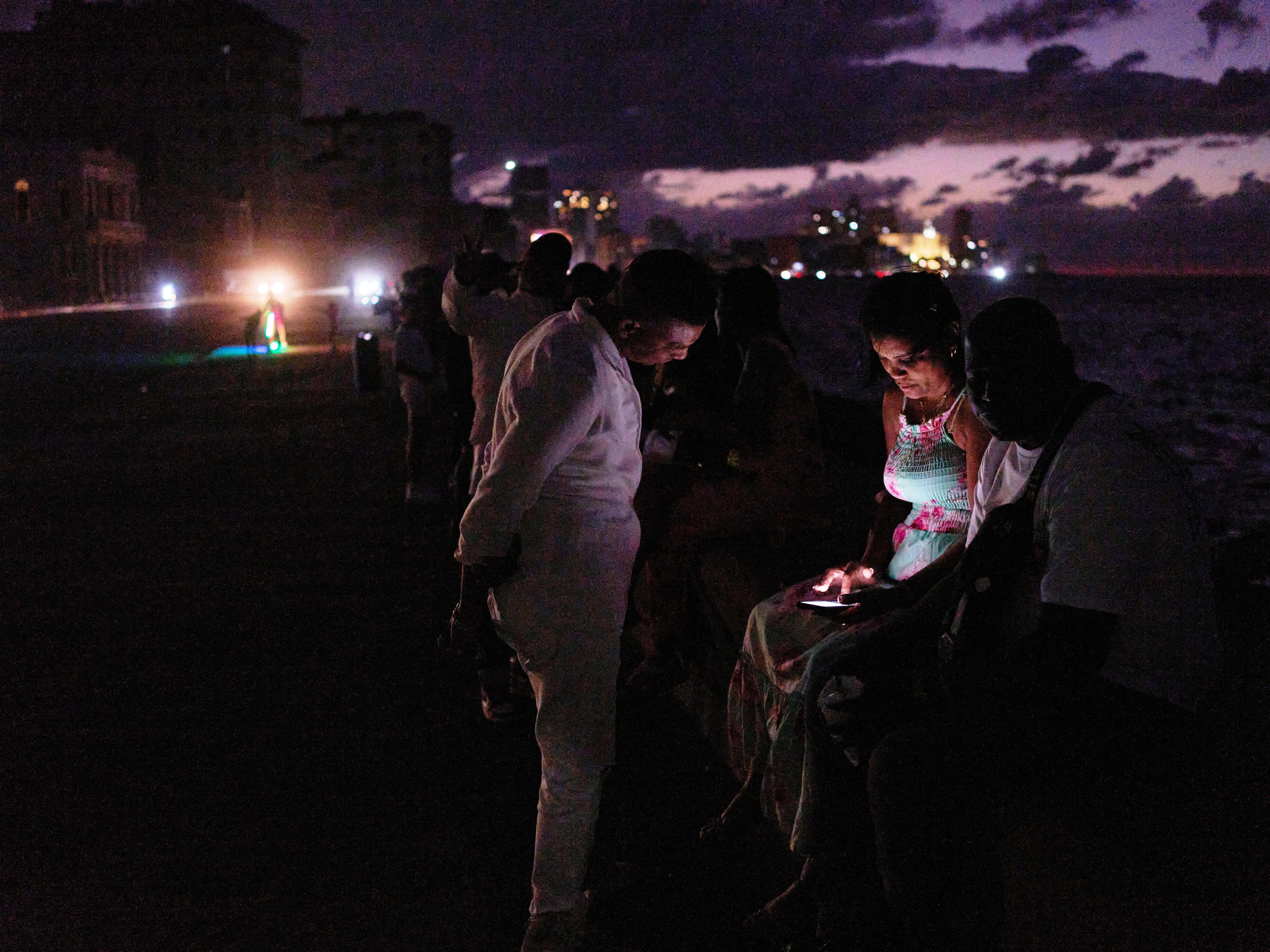 caption: People spend the night in the dark on the Malecon during a blackout in Havana, Cuba, Saturday, March 21, 2026.