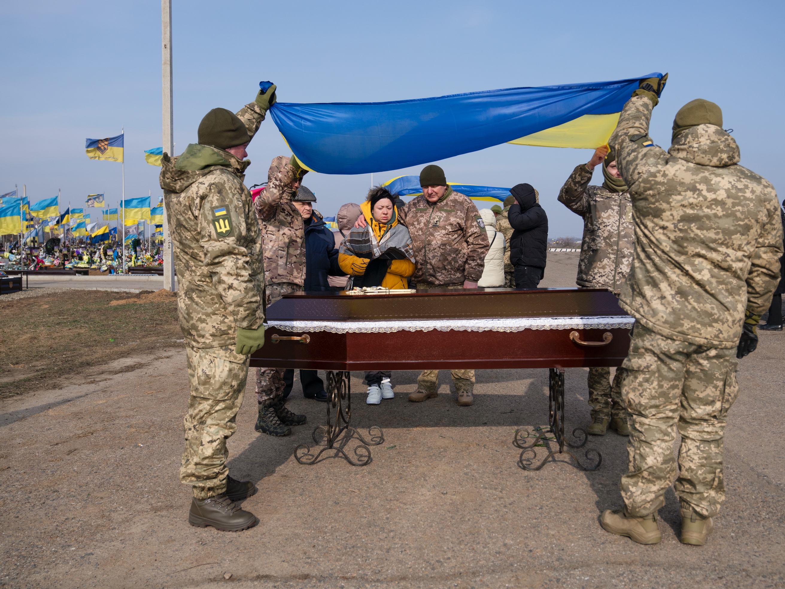 caption: Stanislava Lisovska, 40, (center left) stands at her husband Andrii Ruban's casket (who was killed at 41 years old) with soldiers from his unit, as they bury him in Odesa in February. Ruban a new father when Russia launched its full-scale invasion of Ukraine in February 2022, but like many in those early days, he volunteered to join the army and had been fighting ever since.