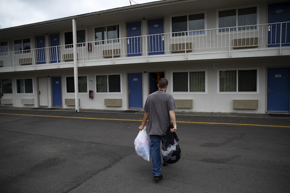caption: Sean carries the family's belongings into their room at a Motel 6, after a fire tore through their apartment complex, on Friday, August 26, 2022. 